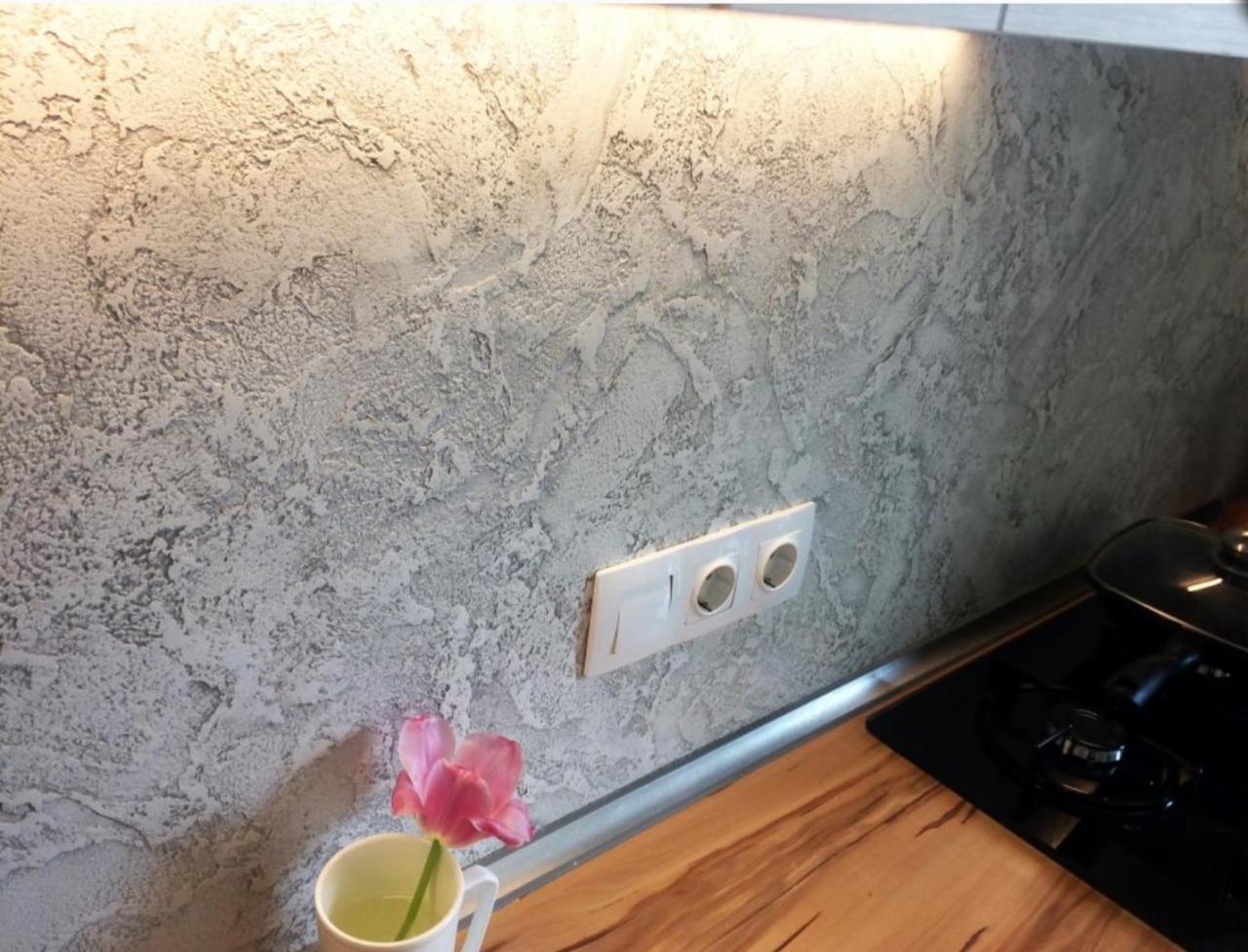 Dekoracyjna ściana w kuchni z efektem strukturalnym w odcieniach szarości, z widocznym gniazdkiem elektrycznym, blatem i tulipanem w kubku.