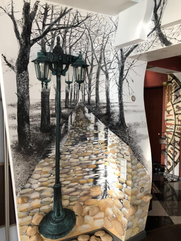 Iluzjonistyczne malowidło ścienne przedstawiające parkową alejkę z latarnią, wykonane w technice mieszanej: czarno-biały rysunek drzew i perspektywy alei przechodzi w trójwymiarową imitację...