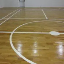 Błyszcząca, drewniana podłoga hali sportowej z wyraźnie oznaczonymi białymi liniami boiska, widok z niskiej perspektywy, ukazujący charakterystyczny okrąg i linie boczne.