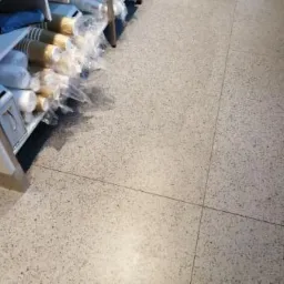 Świeżo umyta, jasna posadzka lastryko w biurze, obok regał z zapasem mopów i środków czystości.