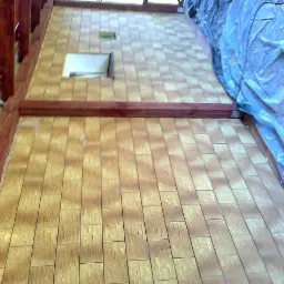 Kafelkowana ściana zewnętrzna budynku z oknem, częściowo zakryta folią ochronną, widok z dołu.