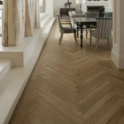 Jasny parkiet ułożony w jodełkę francuską w eleganckim wnętrzu z kolumnami imitującymi drewno i meblami w stylu klasycznym.