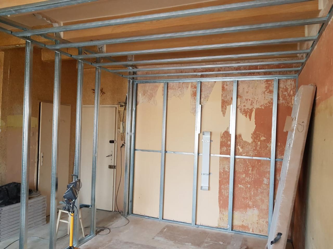 Wnętrze w trakcie prac: metalowa konstrukcja ścian działowych i sufitu podwieszanego, widoczne stare powłoki ścian, przygotowanie do dalszych prac wykończeniowych.