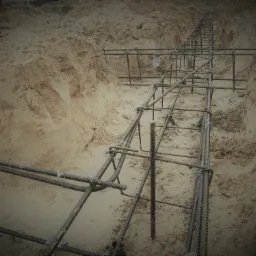 Zbrojenie fundamentów w wykopie z piaskową ziemią, widok z góry w dół wykopu.