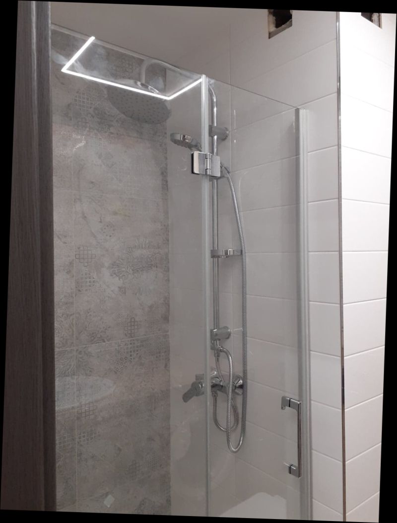 Nowoczesna kabina prysznicowa z chromowaną armaturą, szklanymi drzwiami i dekoracyjnymi szarymi płytkami na ścianie w tle.