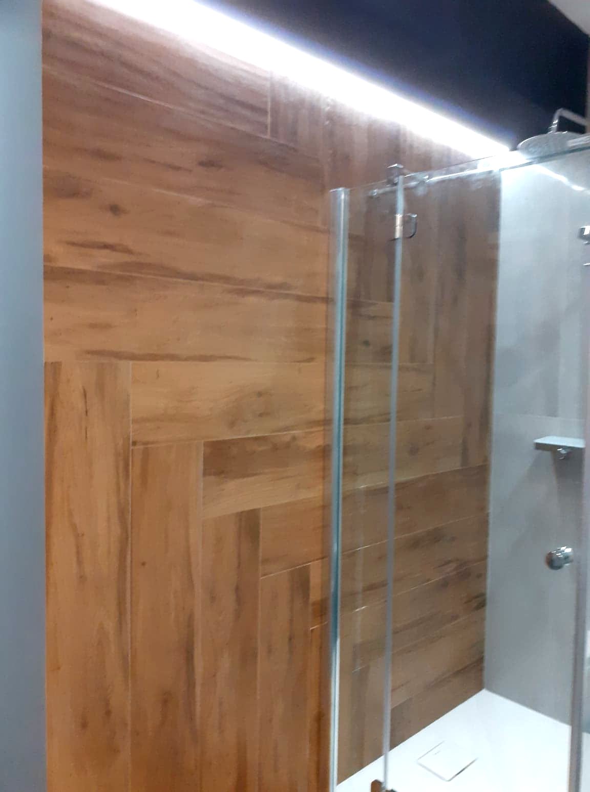 Kabina prysznicowa z drewnopodobnymi płytkami ułożonymi w jodełkę na ścianie, oświetlenie LED podsufitowe.