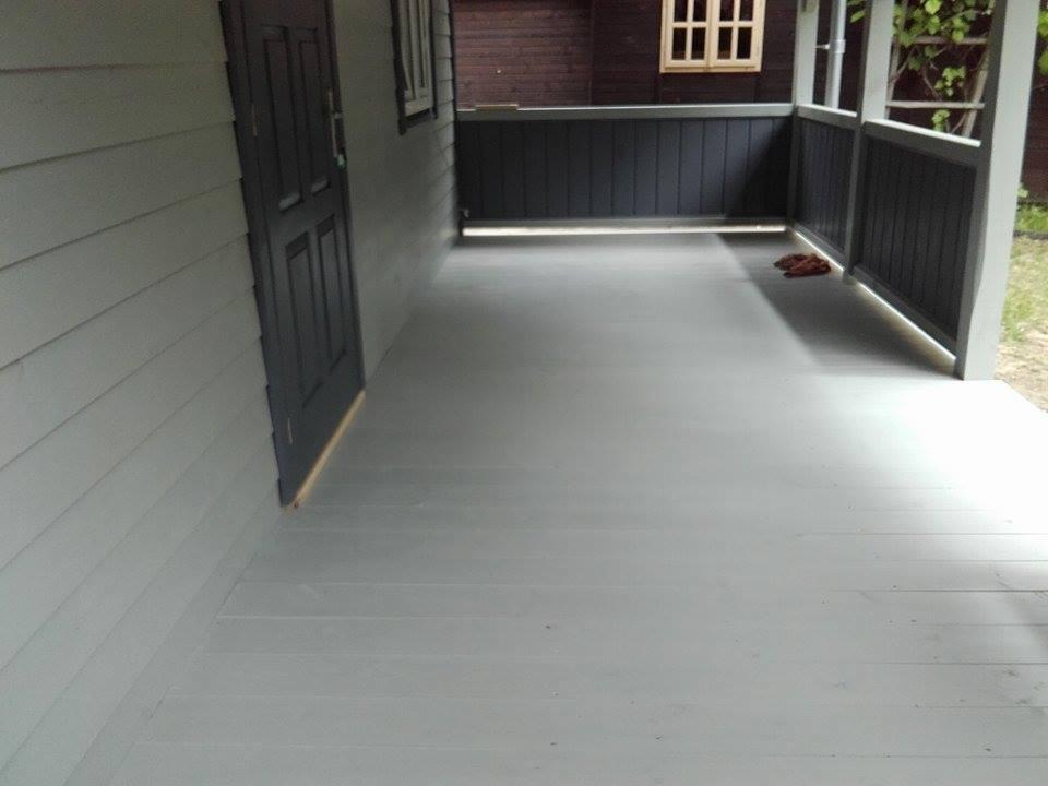 Szary, drewniany taras przy domu w Długosiodle, z widoczną konstrukcją balustrady i ścianą budynku z ciemnymi drzwiami.