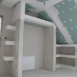 Szkielet zabudowy szafy wnękowej z płyt kartonowo-gipsowych w surowym stanie, widoczne niedoskonałości gładzi i połączeń, fragment poddasza ze skośnym sufitem i płytami GK.