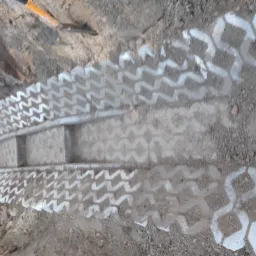 Przygotowanie podłoża pod ułożenie ażurowych płyt betonowych z widocznym wykopem i łopatą w tle.