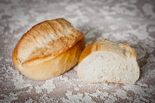 Kromka chleba i przekrojona bułka pszenna na blacie posypanym mąką, widok z góry.