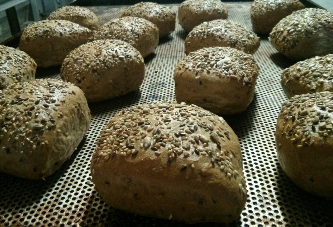 Świeżo upieczone, brązowe bułki posypane mieszanką ziaren leżą na perforowanej blasze do pieczenia.