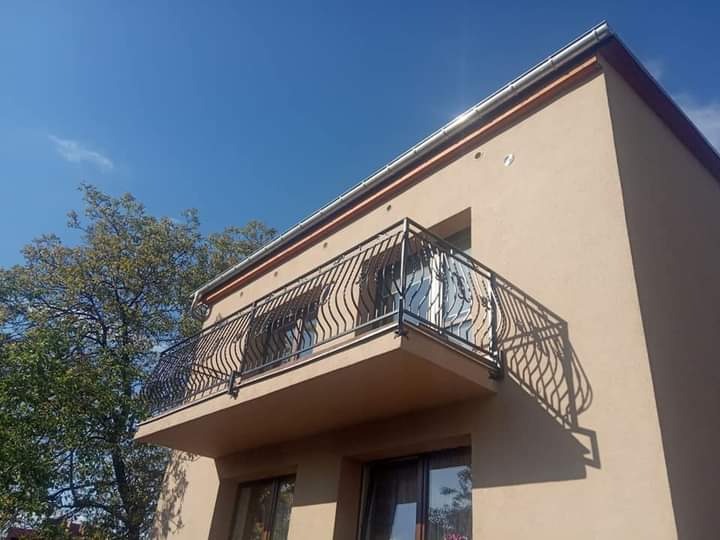 Kuta balustrada balkonowa z motywem roślinnym, zamontowana na budynku w kolorze beżowym, widok z dołu pod kątem.