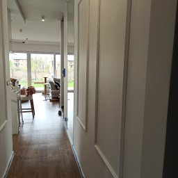 Jan Wądolny - Korytarz w trakcie prac przygotowawczych do malowania, ściany zabezpieczone taśmą malarską, widoczne listwy dekoracyjne i parkiet.