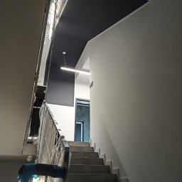 Jan Wądolny - Klatka schodowa w biurze w trakcie prac wykończeniowych, ściany pomalowane na biało, sufit częściowo na czarno, zabezpieczona folią barierka schodów.