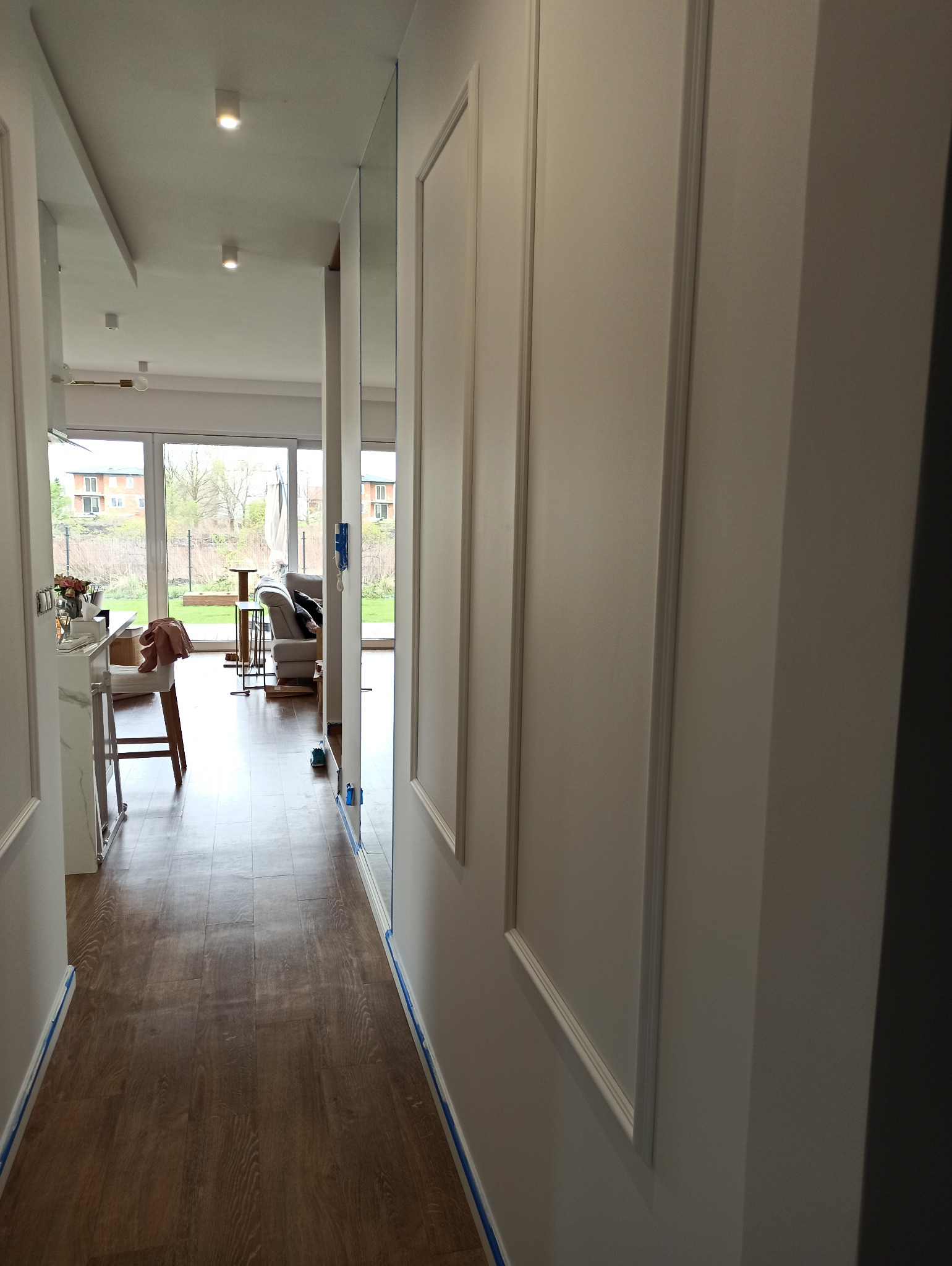 Korytarz w trakcie prac przygotowawczych do malowania, ściany zabezpieczone taśmą malarską, widoczne listwy dekoracyjne i parkiet.