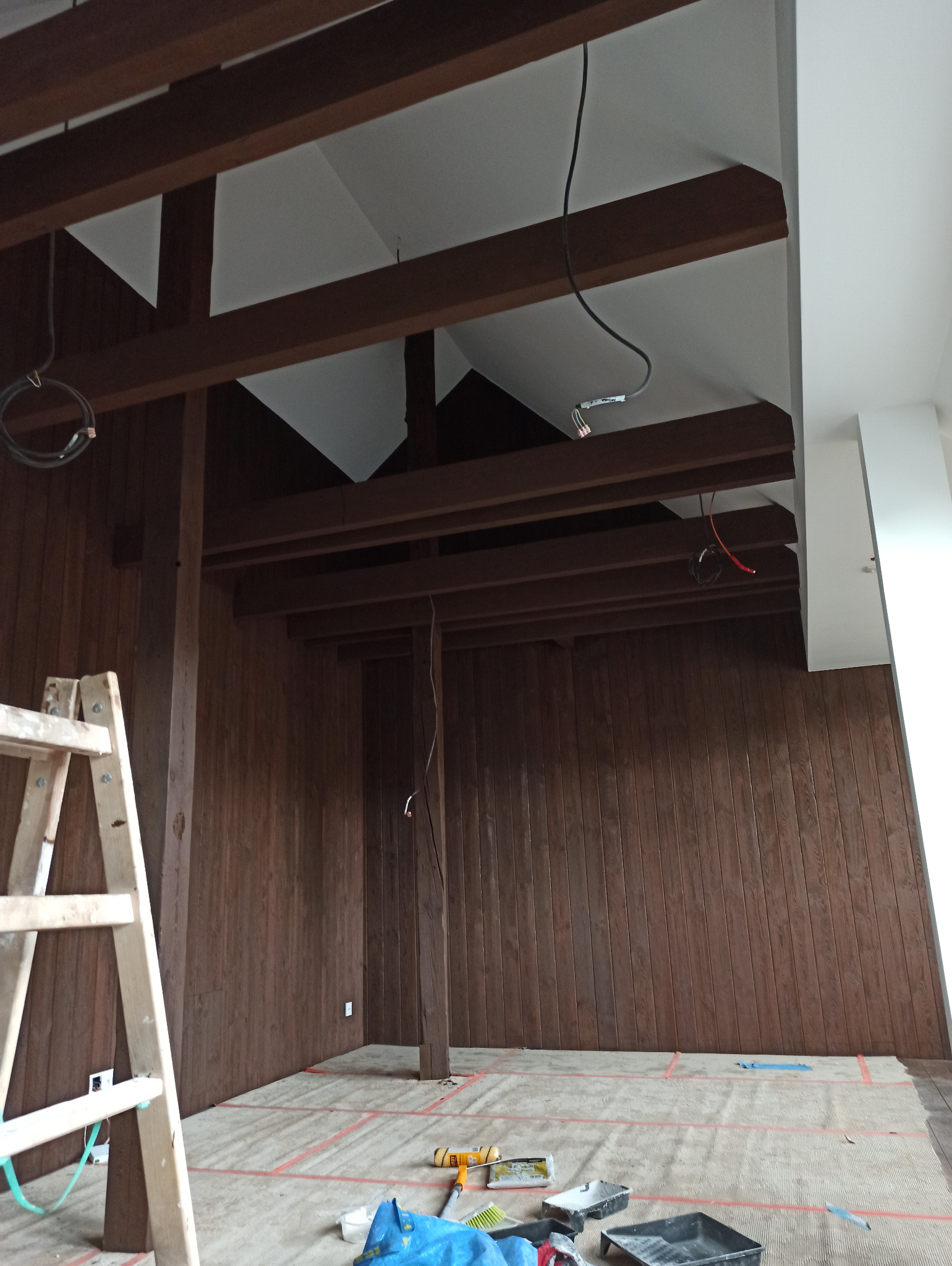 Wnętrze biura z drewnianą boazerią w trakcie przygotowań do malowania, widoczna drabina, zabezpieczona podłoga i narzędzia malarskie.