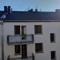 Nowo wybudowany budynek wielorodzinny z balkonami i ciemną dachówką, widok z góry na elewację i fragment dachu.