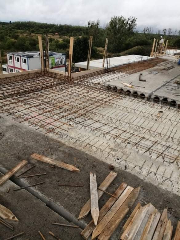 Zbrojenie stropu w trakcie budowy domu, widoczne elementy szalunku i pręty zbrojeniowe ułożone na betonowych płytach stropowych, w tle zabudowa kontenerowa.