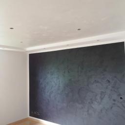 Malert - Ściana w odcieniach szarości z dekoracyjną fakturą w Oławie, widoczne gniazdka elektryczne i drewniana podłoga.