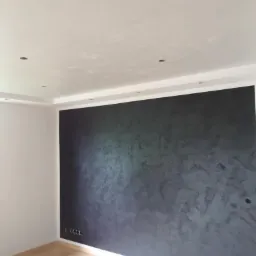 Ściana w odcieniach szarości z dekoracyjną fakturą w Oławie, widoczne gniazdka elektryczne i drewniana podłoga.