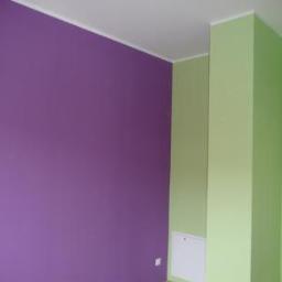 Malert - Pomieszczenie po remoncie: ściana w kolorze fioletowym kontrastuje z jasnozieloną ścianą i filarem, widoczna biała listwa przysufitowa i biały panel rewizyjny.