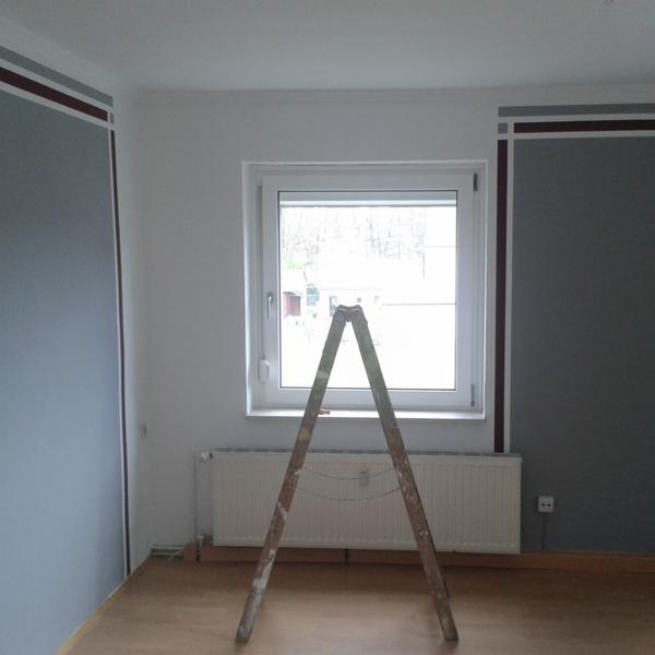 Pokój po odświeżeniu ścian, widoczne pomalowane ściany w dwóch odcieniach szarości z bordowymi akcentami, drewniana podłoga, białe okno i drabina malarska