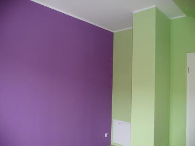 Pomieszczenie po remoncie: ściana w kolorze fioletowym kontrastuje z jasnozieloną ścianą i filarem, widoczna biała listwa przysufitowa i biały panel rewizyjny.