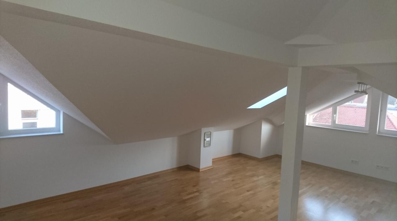 Poddasze po remoncie: świeżo pomalowane białe ściany i sufit, jasna drewniana podłoga, okna dachowe i szczytowe, widok na zewnątrz.