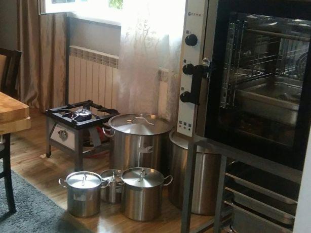 Profesjonalny piec konwekcyjny, garnki ze stali nierdzewnej z pokrywkami, kuchenka gazowa na metalowym stojaku w pomieszczeniu.