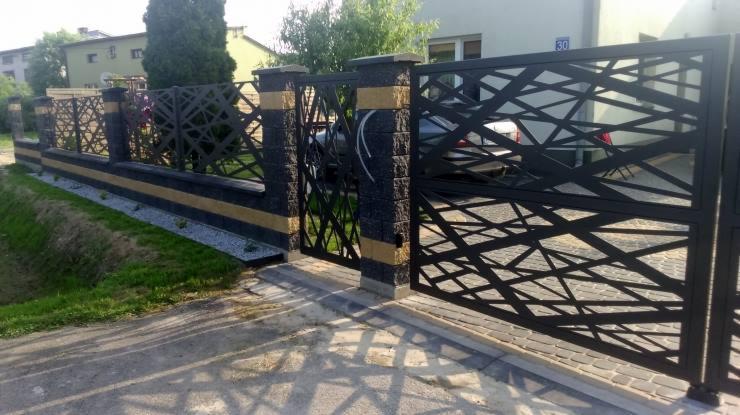 Nowoczesne ogrodzenie i brama w kolorze antracytowym z geometrycznym wzorem, słupki z elementami dekoracyjnymi w kolorze piaskowym, widok na posesję.