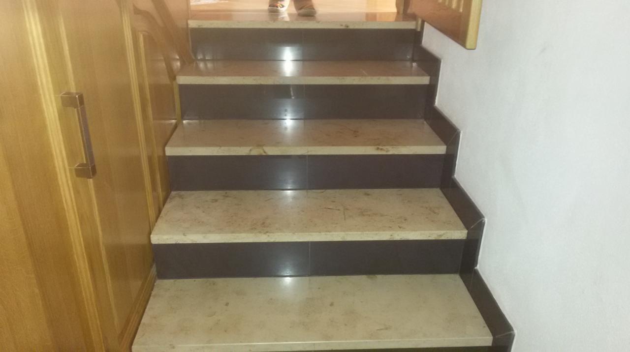 Schody wewnętrzne wyłożone beżowym marmurem z ciemnobrązowymi podstopnicami, widoczne fragmenty drewnianej szafy z chromowanym uchwytem i białej ściany.