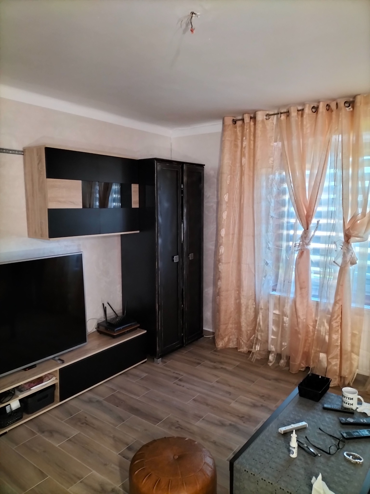 Umeblowany pokój dzienny z czarno-beżową zabudową meblową, brązową pufą i transparentnymi zasłonami w odcieniach brzoskwini, ukazujący efekt aranżacji wnętrza.