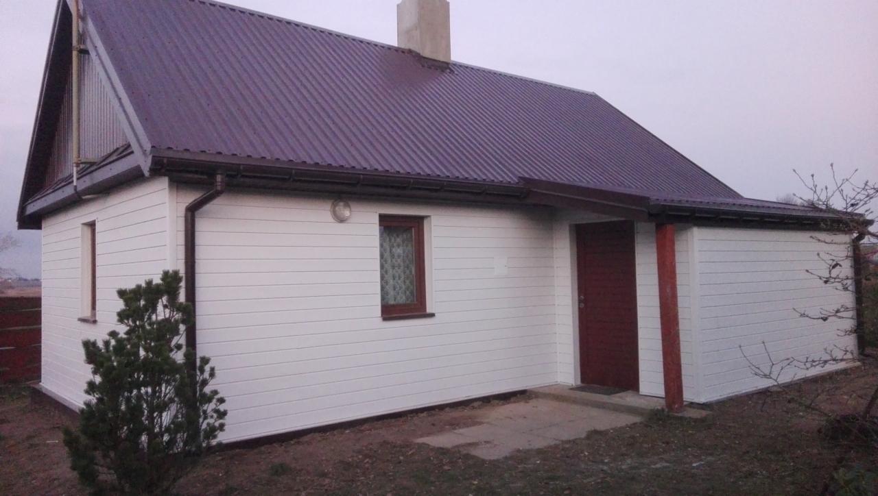 Dom jednorodzinny z białą elewacją panelową, ciemnobrązowym dachem z blachy trapezowej i brązowymi rynnami, widoczny z zewnątrz w pochmurny dzień.