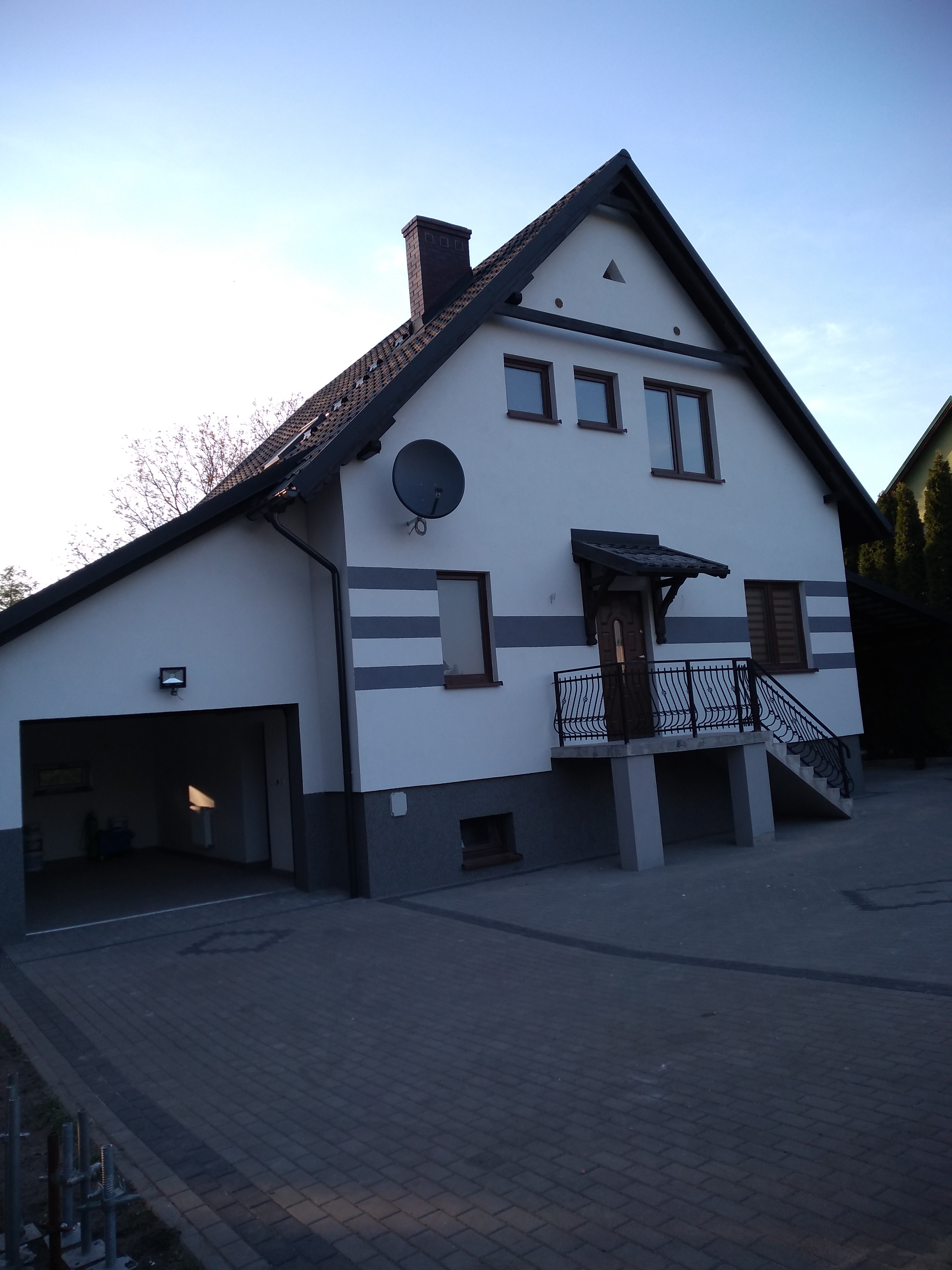 Dwupiętrowy dom jednorodzinny z garażem, świeżo pomalowany na biało z szarymi poziomymi pasami, czarnym dachem i detalami, widoczny z zewnątrz na tle błękitnego nieba.