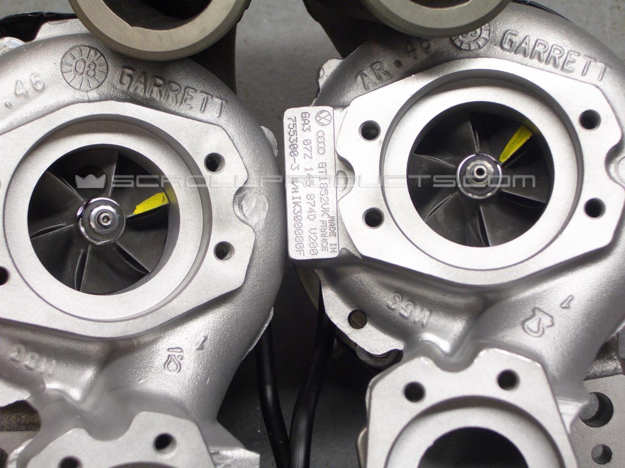 Dwa nowe, srebrne turbosprężarki Garrett, z widocznymi numerami seryjnymi i oznaczeniami producenta, ustawione obok siebie na szarym tle. Na jednym ze sprężarek widoczna żółta naklejka na łopatkach...