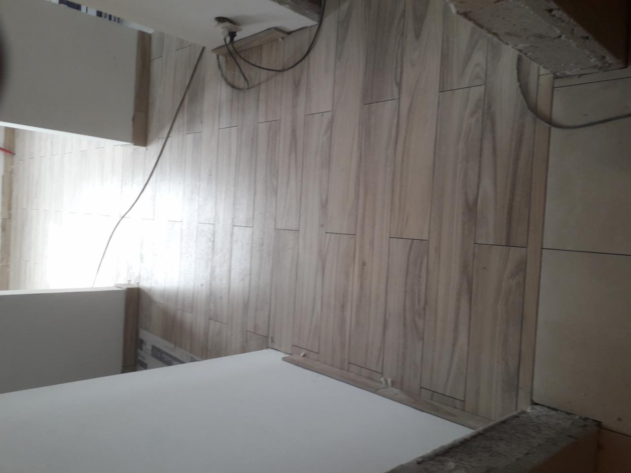 Ułożone panele podłogowe o wzorze drewna w jasnym odcieniu, widoczne fragmenty ścian i narożników pomieszczenia, przewody elektryczne przy suficie.