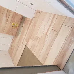 Układanie płytek imitujących drewno na podłodze w Tarnowie, widoczne krzyżyki dystansowe i przygotowane otwory na instalacje.