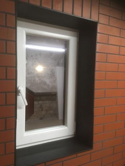 Okna PCV wstawione w mur z cegły, z widocznym wnętrzem w trakcie prac wykończeniowych.