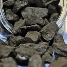 Błyszczące bryłki węgla kamiennego wysypujące się z przechylonego słoika na niebieskie tło.