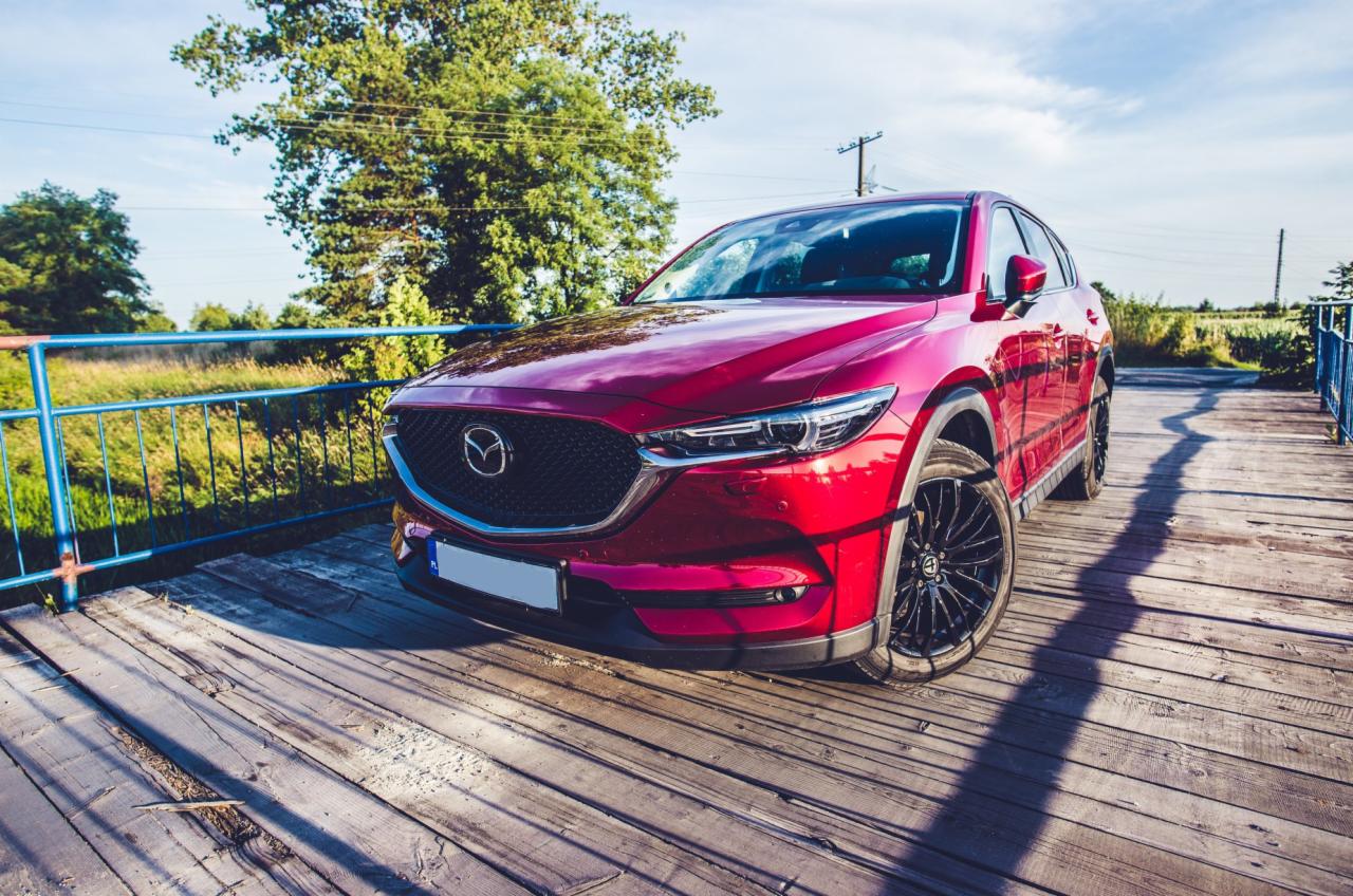 Czerwona Mazda CX-5 na drewnianym moście z niebieską barierką, widok z przodu, letnie słońce.