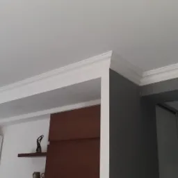 Białe listwy dekoracyjne na styku ściany i sufitu w jasnym wnętrzu, widoczne detale wykończenia i oświetlenia.