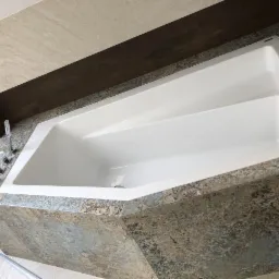 Nowoczesna, biała wanna obudowana płytkami w stylu vintage, z chromowaną armaturą i drewnianym panelem nad nią, widok z góry.