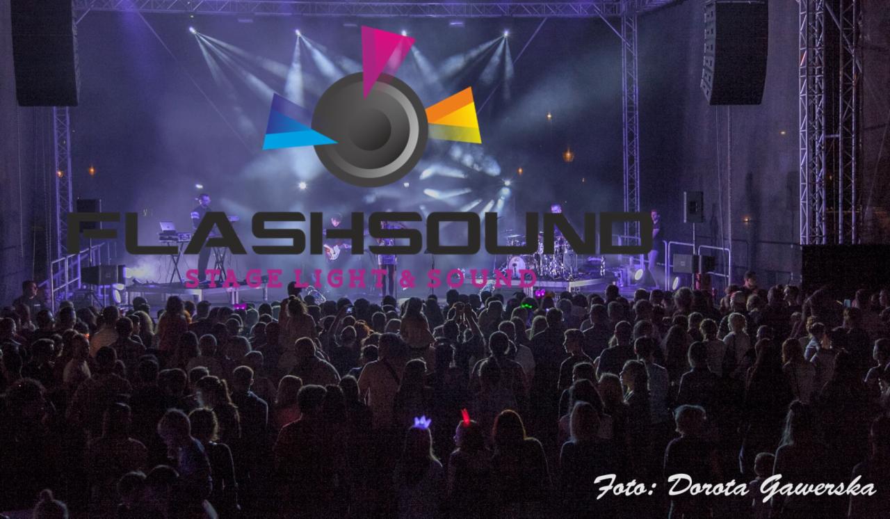Koncert plenerowy: tłum ludzi przed sceną, na której widać muzyków i sprzęt, nad nimi logo firmy Flashsound Stage Light & Sound, całość oświetlona reflektorami, w prawym dolnym rogu podpis autora...