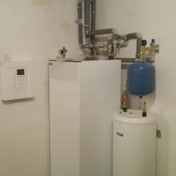 Biały piec centralnego ogrzewania z szarymi rurami instalacji hydraulicznej w pomieszczeniu w Pabianicach.