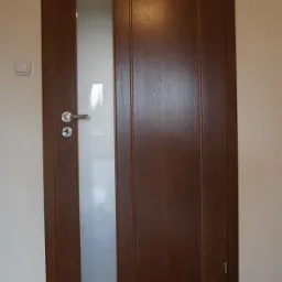 Brązowe skrzydło z matowym przeszkleniem, chromowana klamka, widoczny fragment parkietu.