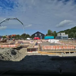 Wykonywanie fundamentów pod dom w Adamowie: szalunki zbrojeniowe przygotowane do zalewania betonem, widoczny dźwig z pompą do betonu.