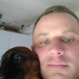 kamilotrans - Mężczyzna z niebieskimi oczami obejmuje szczeniaka z brązową sierścią na tle białego sufitu z oświetleniem.