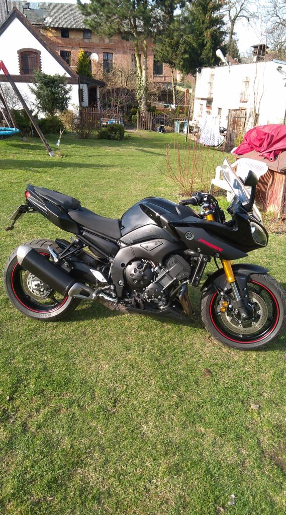 Czarny motocykl sportowo-turystyczny zaparkowany na trawniku przed domem jednorodzinnym.