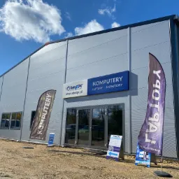 Budynek firmy komputerowej IntexPC z szyldem i flagami reklamowymi na zewnątrz, widoczny samochód dostawczy.