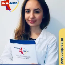 Portret uśmiechniętej kobiety w białym fartuchu medycznym, trzymającej w rękach folder z logo i nazwą 'Health Inn Med' oraz informacją 'Dietetyka i żywienie medyczne'. W tle widoczne logo firmy.